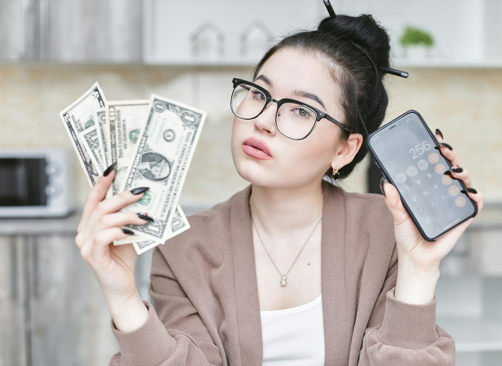 Woman holding cash and smartphone displaying calculator, highlighting personal finance management.