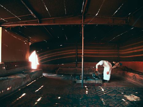 A Bedouin man in traditional attire inside a dimly lit tent with sunbeams creating patterns.
