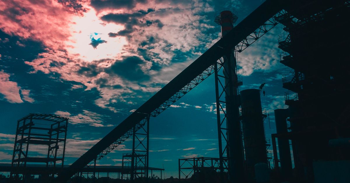 Silhouetted industrial structures at sunset with vibrant clouds in West Kalimantan, Indonesia.