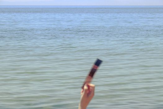 A hand holding photographic film against a sea horizon on a clear day.