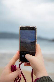 A person capturing a beach scene on a smartphone with blurred background.