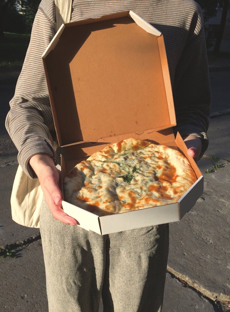 A Person Holding A Box Of Pizza