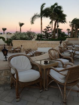 Serene outdoor lounge area with wicker furniture and palm trees at sunset, ideal for travel and leisure imagery.