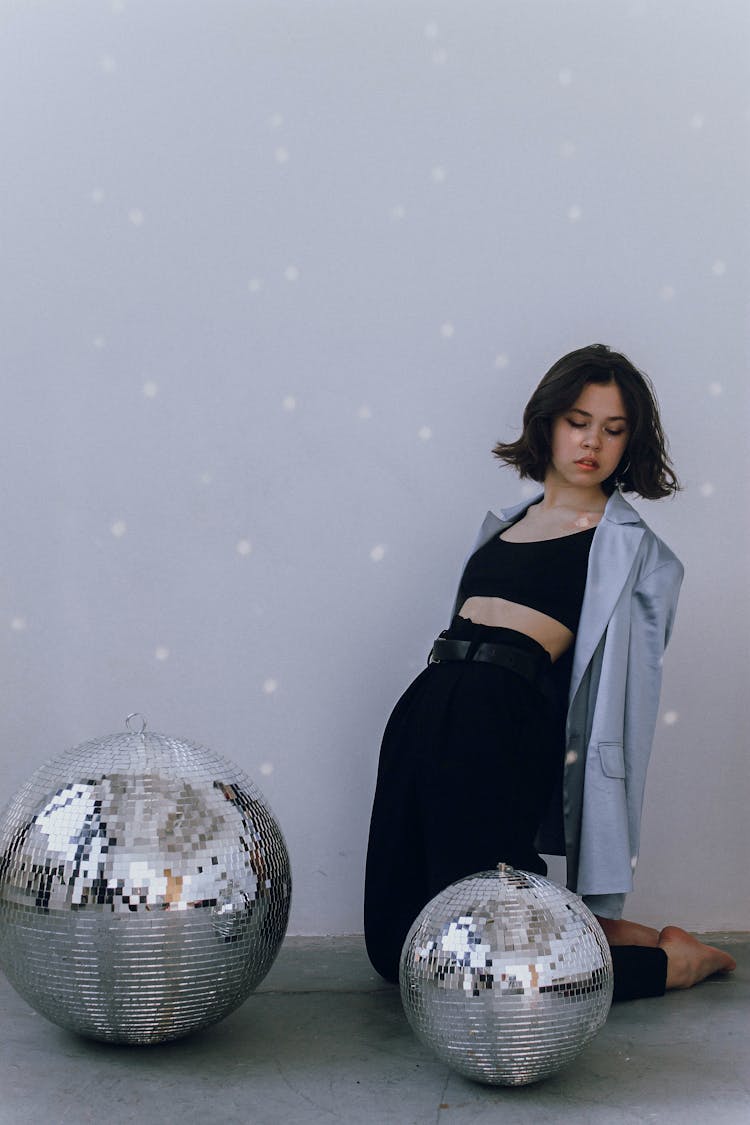 Young Woman Sitting Near Shining Disco Balls