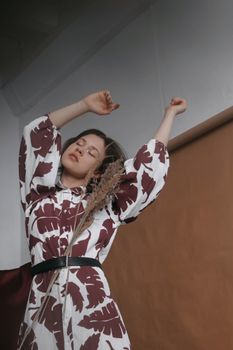 Young woman in a patterned dress posing with closed eyes, showcasing elegance and fashion indoors.