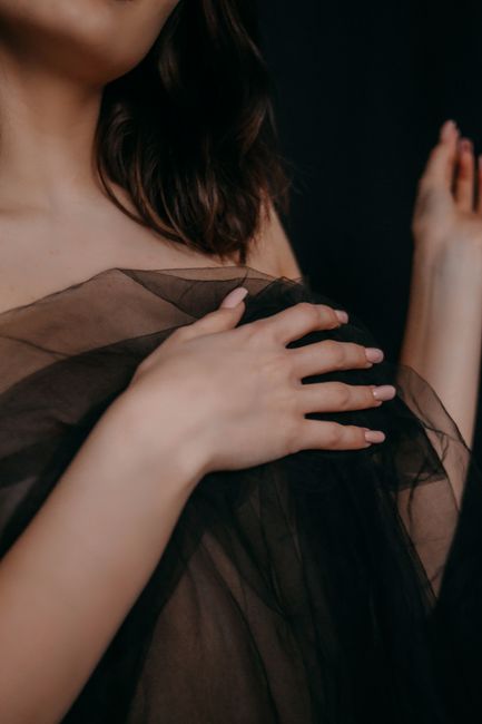 Close-up of a woman's hand and shoulder draped in sheer black fabric, exuding elegance.