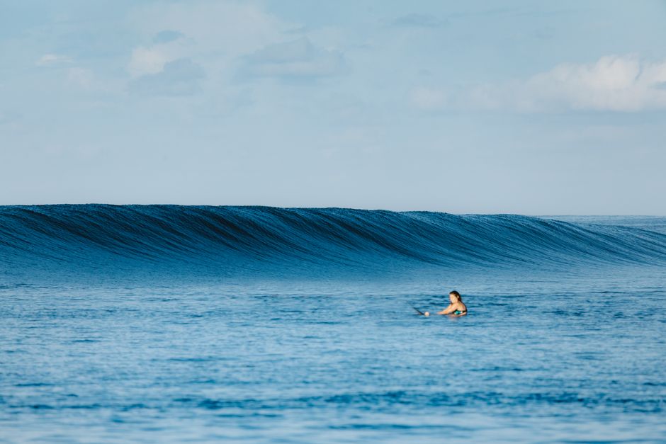A lone surfer paddles in the calm blue ocean with beautiful waves in West Sumatra.