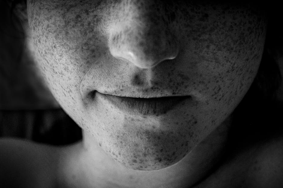 Artistic black and white close-up of a face highlighting freckles and lips.