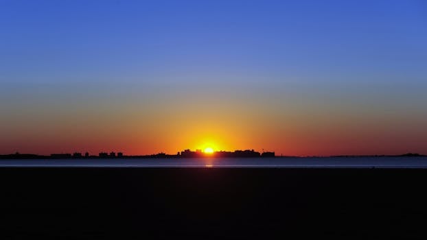 宁静的日落映照在海洋与城市剪影之上，天空混合着充满活力的橙色和深蓝色