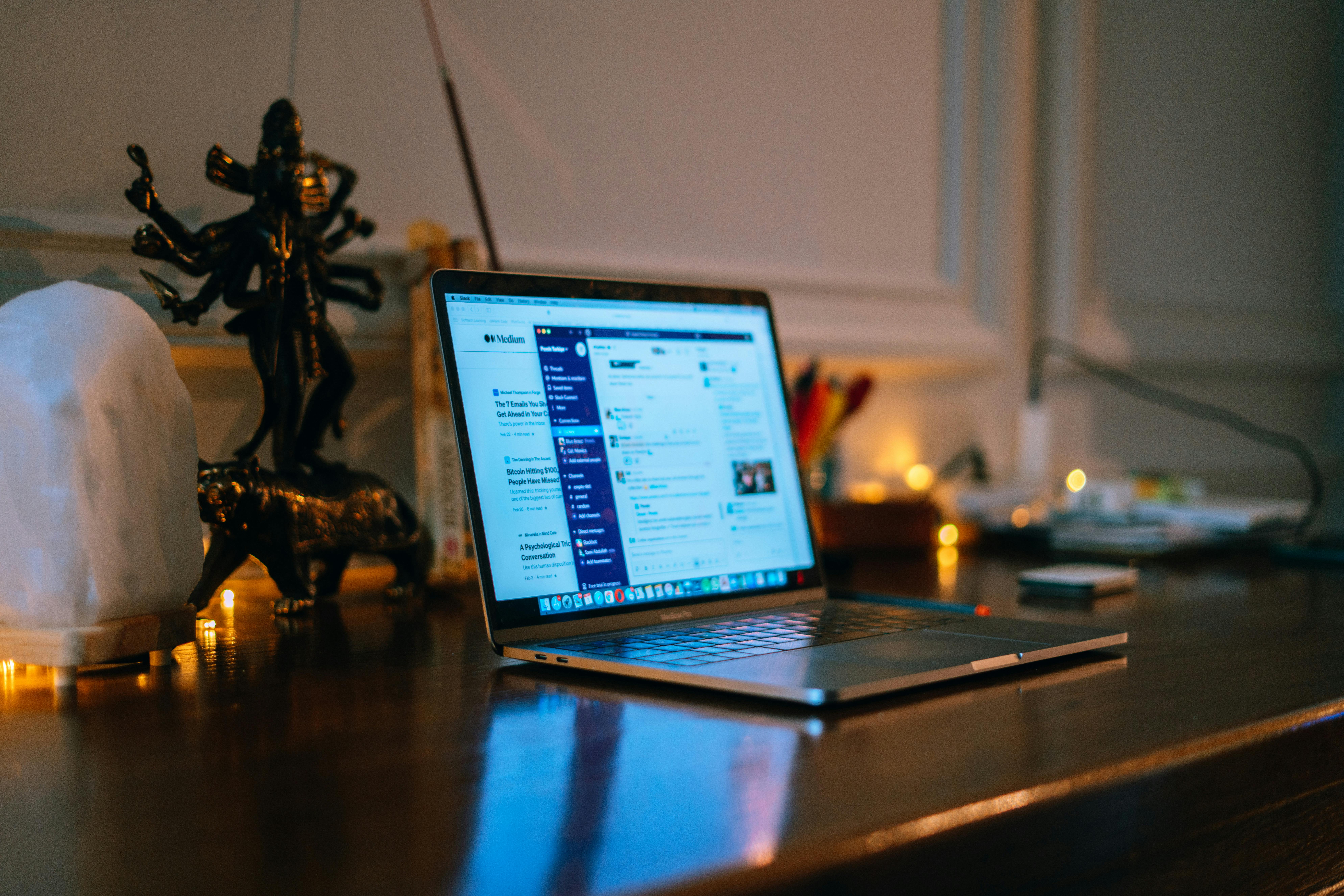 A cozy home office setup with a laptop on a wooden desk surrounded by warm lighting and decor.