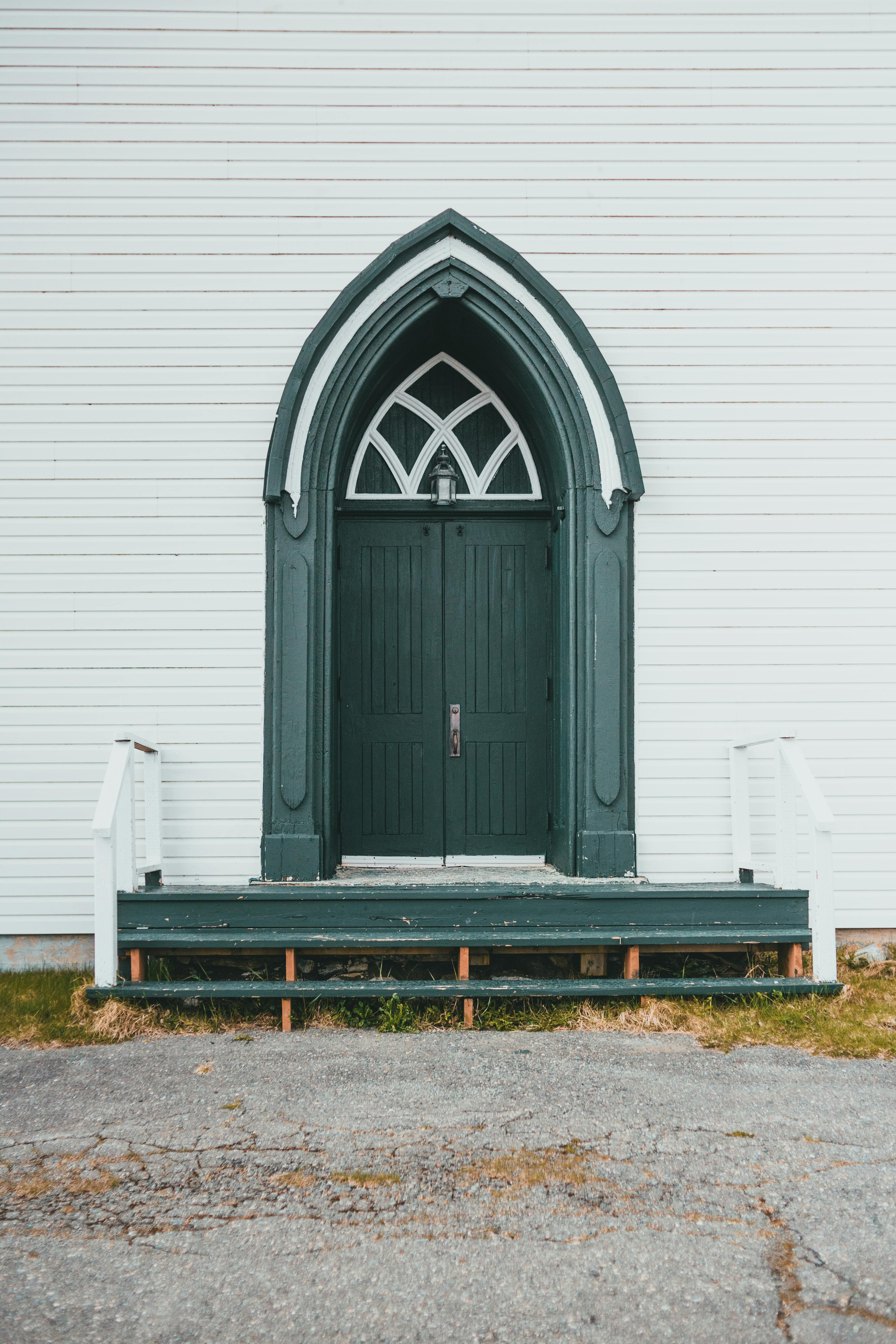 Green arched Gothic doorway on white exterior wall with wooden steps, ideal for architecture themes.