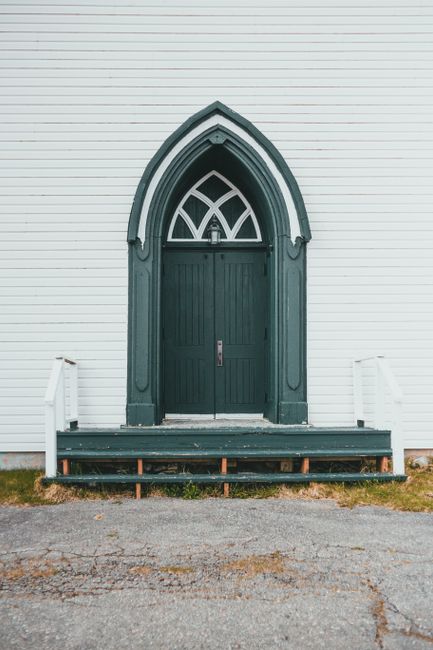 Green arched Gothic doorway on white exterior wall with wooden steps, ideal for architecture themes.