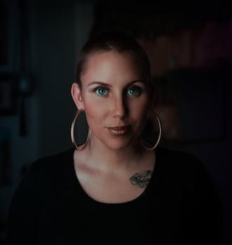 在昏暗的工作室里，一位蓝眼、佩戴大胆耳环的女性肖像散发出自信与风格