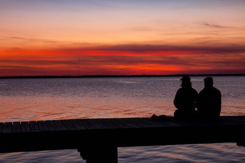 Free A Silhouette of People Sitting on a Dock Stock Photo