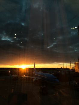 An airplane silhouetted against a vibrant sunset at an airport in Norway.