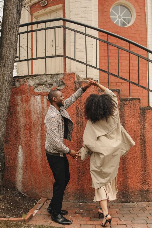Free Happy African American couple dancing joyfully outside near a rustic building wall. Stock Photo