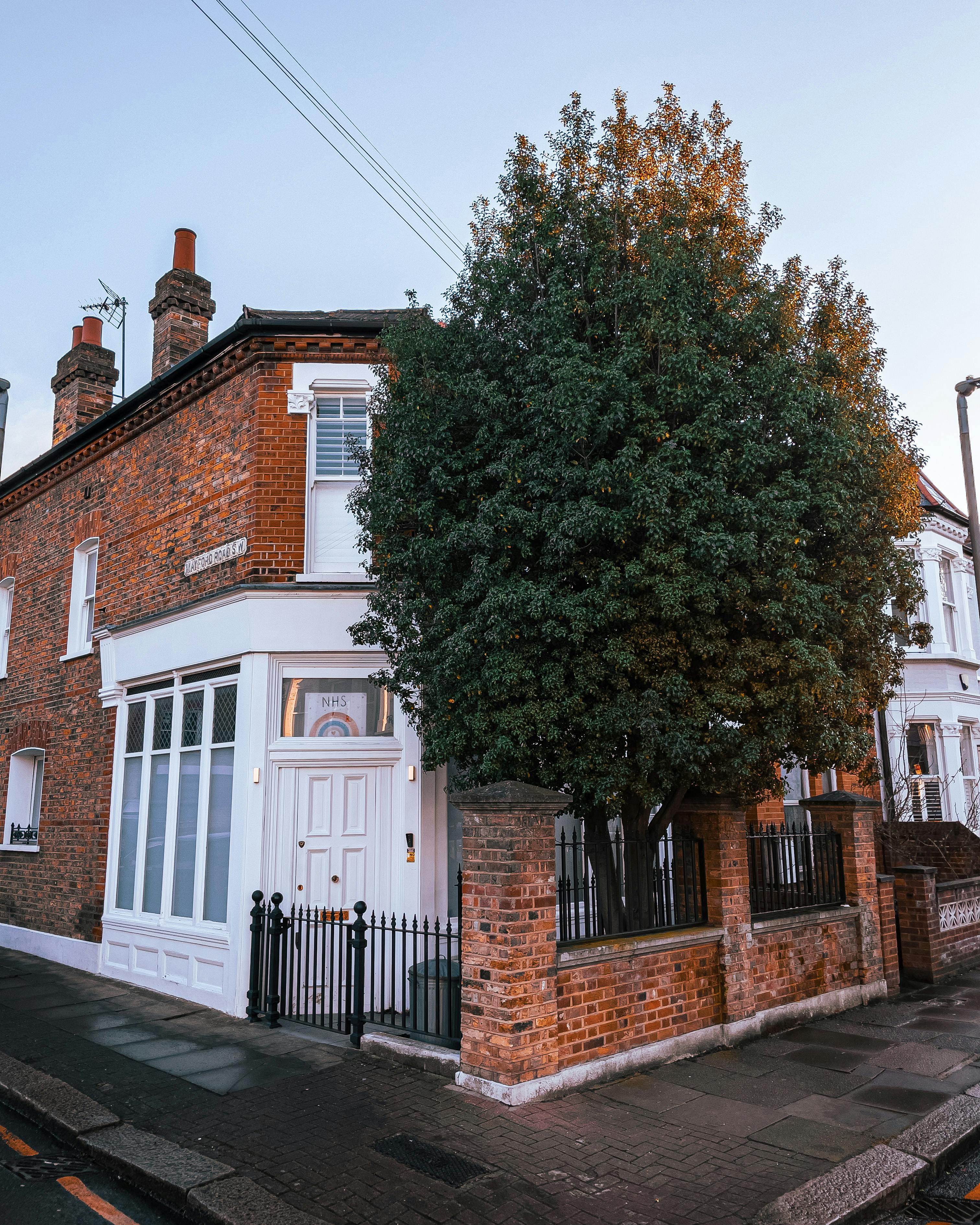 Free A picturesque brick house corner featuring a lush tree, perfect for residential themes. Stock Photo