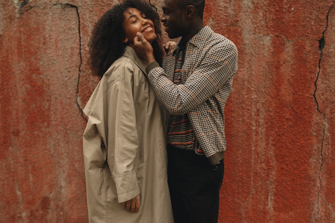 Free Happy Couple Standing Near A Red Wall Stock Photo