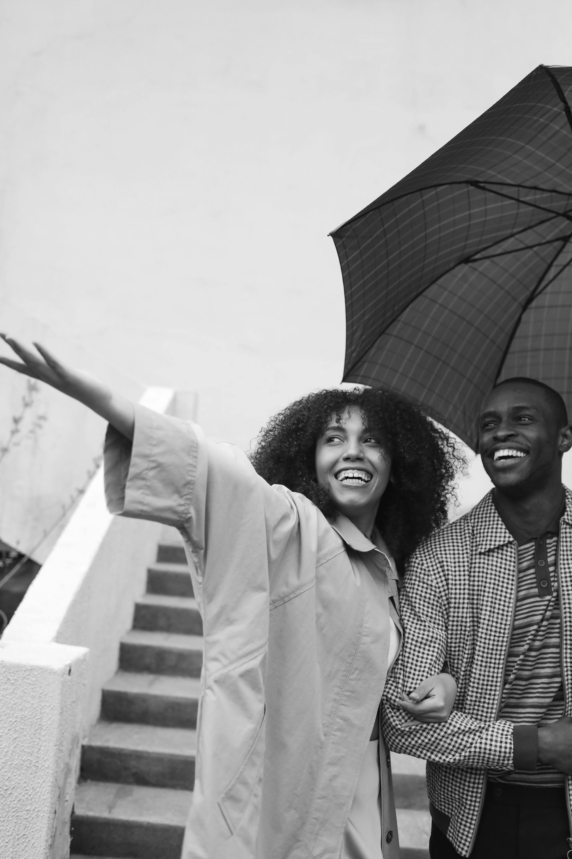 A happy couple sharing a moment under an umbrella in a grayscale outdoor setting.