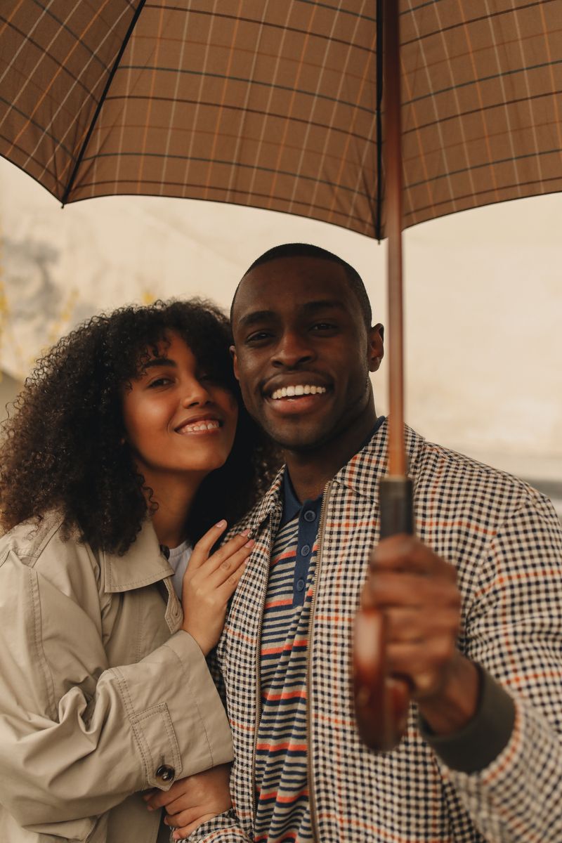 Happy couple smiling under an umbrella on an autumn day — photo by Polina Tankilevitch on Pexels