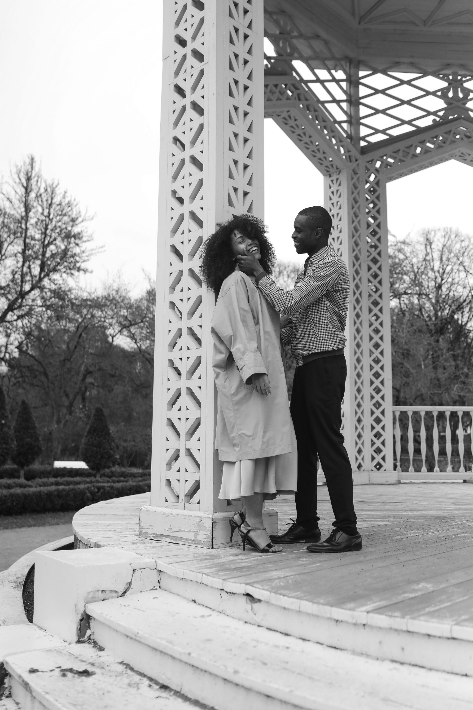 A loving couple enjoys a playful moment in a park gazebo, captured in black and white.