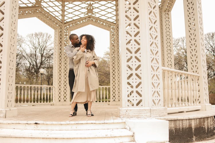 Couple Standing In White Wooden Gazebo