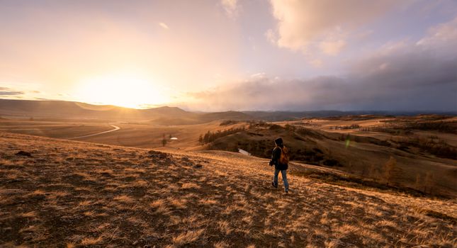 A lone hiker at sunset enjoying a vast, tranquil landscape of rolling hills.