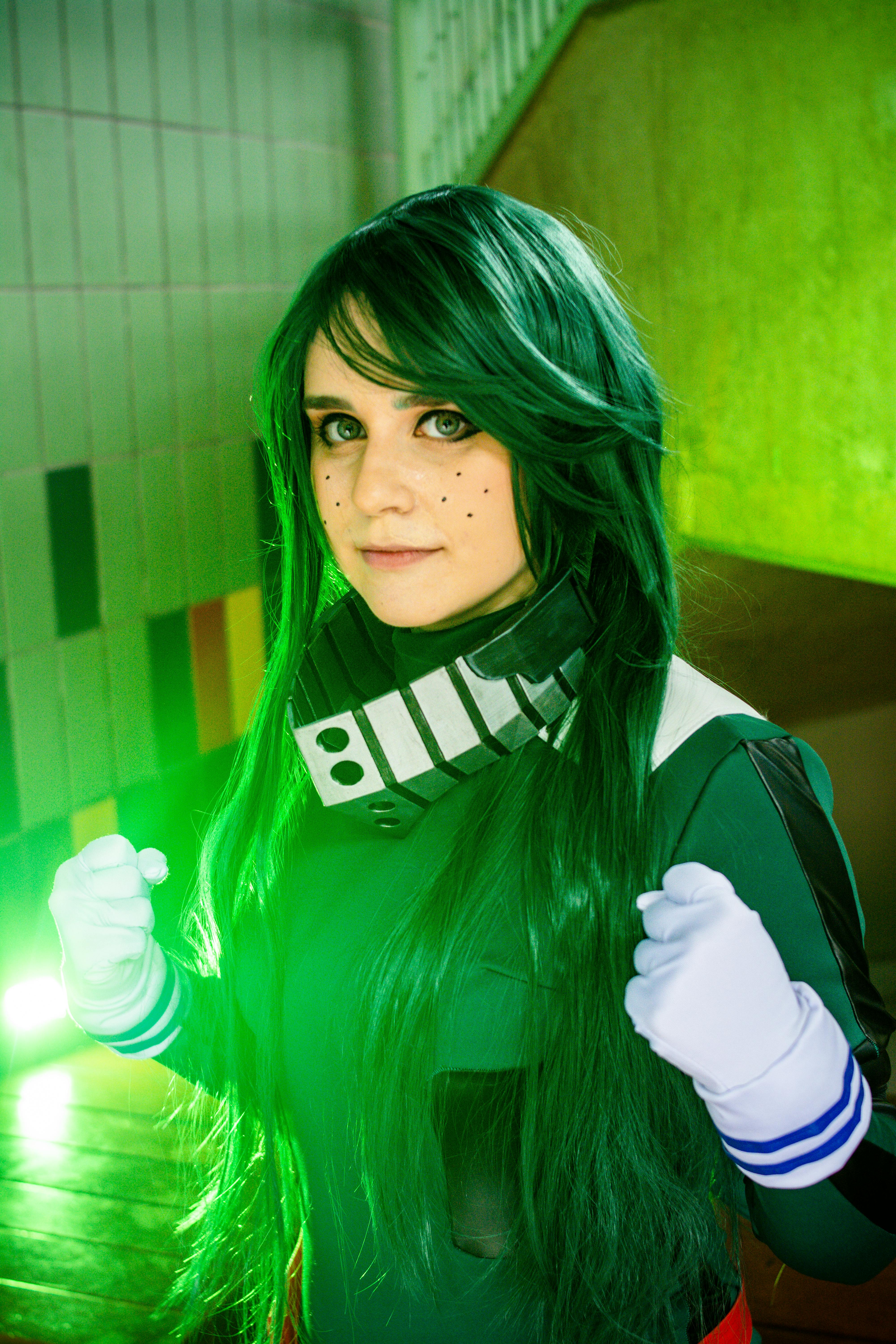Cosplay enthusiast in striking green costume posing confidently indoors.