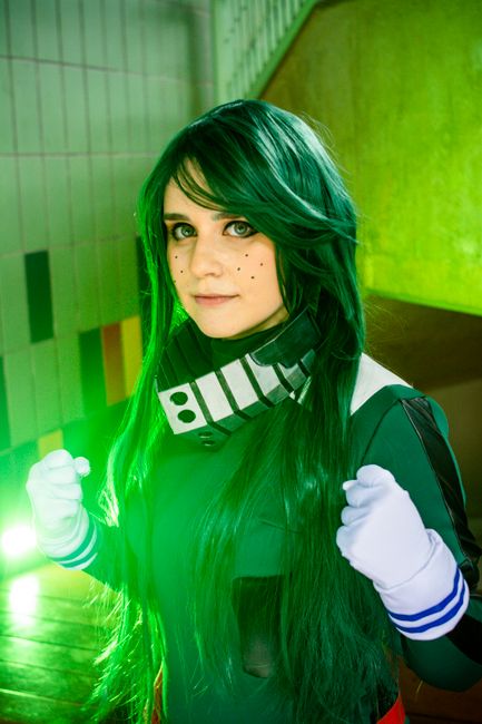 Cosplay enthusiast in striking green costume posing confidently indoors.