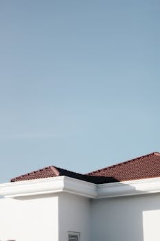 A minimalist view of a modern rooftop with red tiles against a clear blue sky, showcasing architectural elegance.