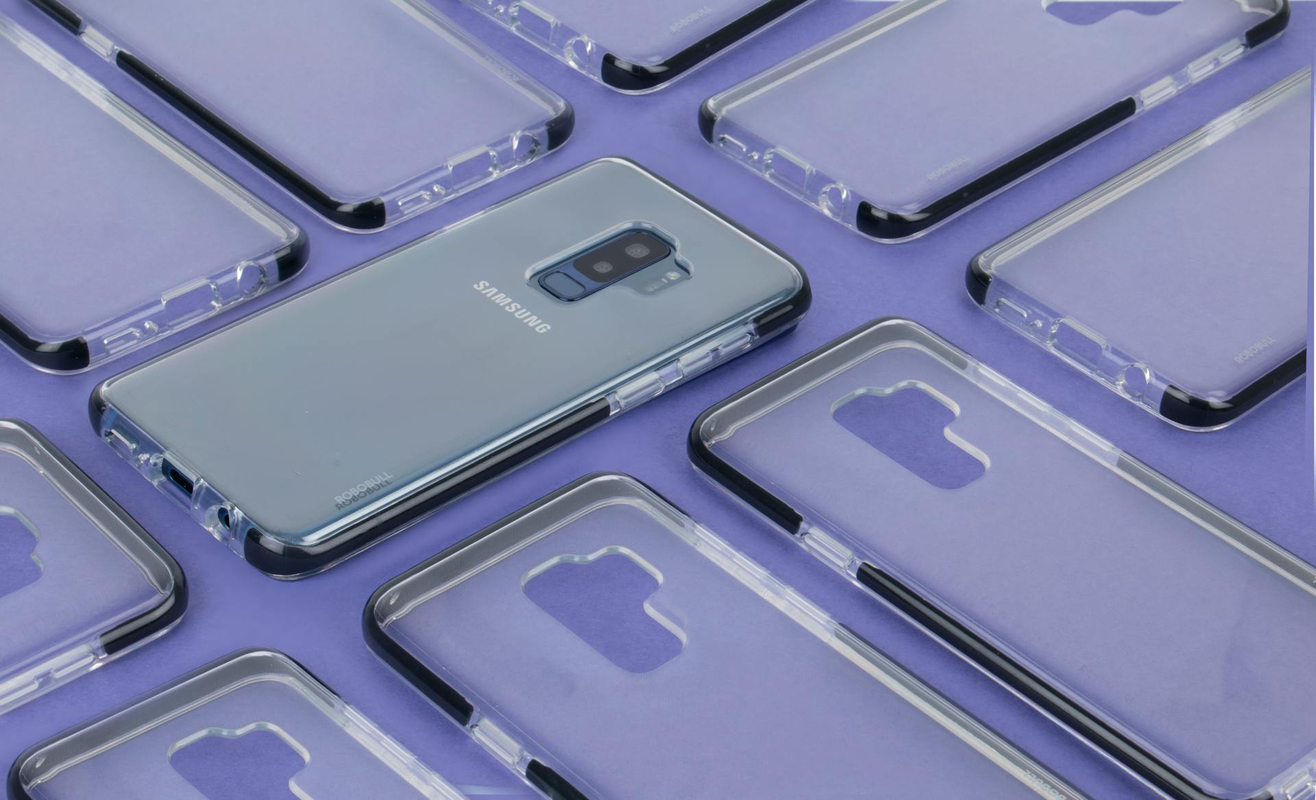 Close-up of a Samsung phone surrounded by transparent cases on a purple surface, showcasing modern technology.