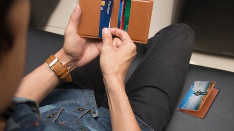 A close-up of a man holding a wallet containing credit cards and an ID inside a room.