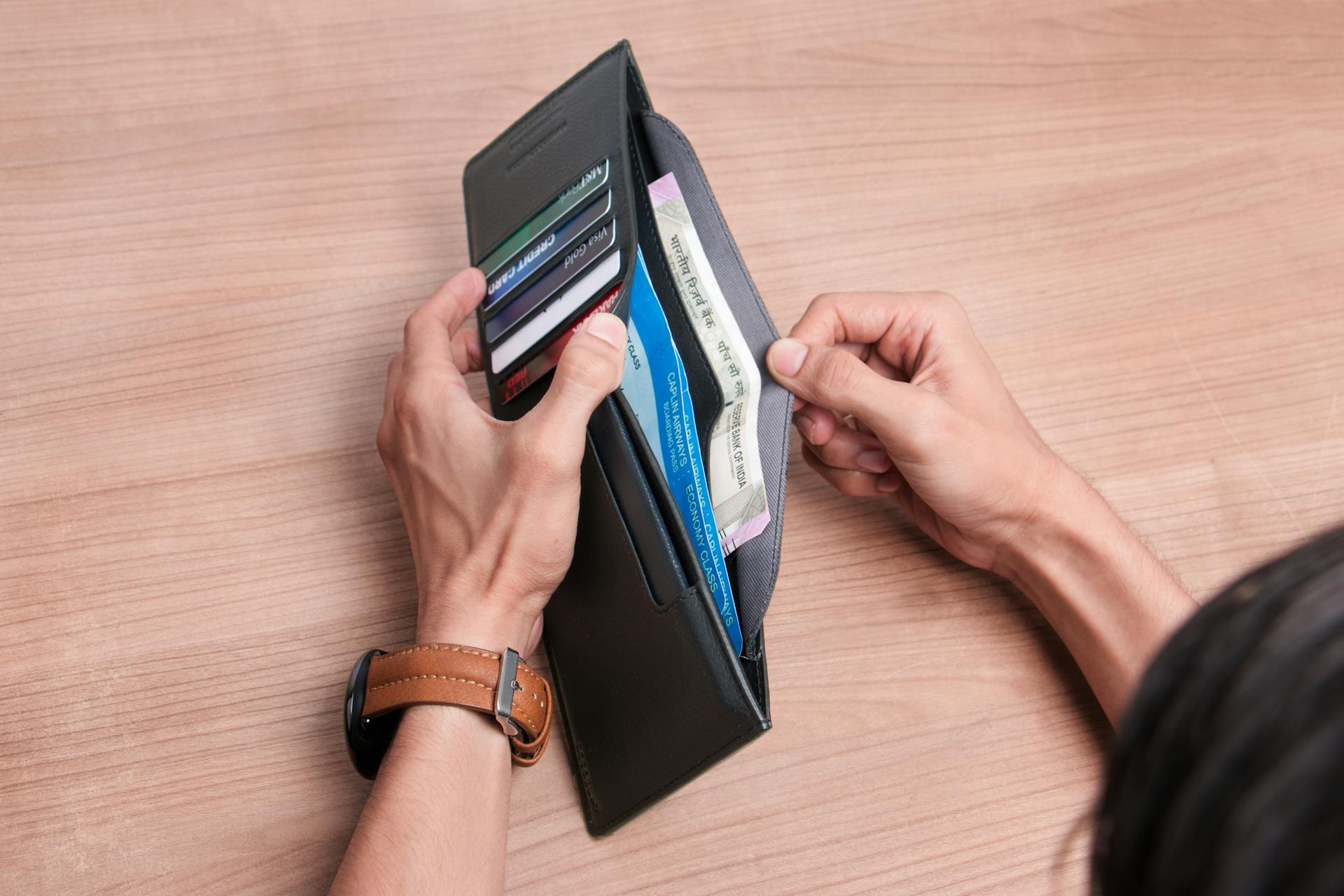 Close-up of a person managing a wallet with cash and cards on a wooden table.