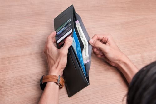 Free Close-up of a person managing a wallet with cash and cards on a wooden table. Stock Photo