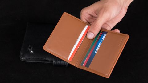 Close-up of a hand holding an open brown leather wallet filled with credit cards.