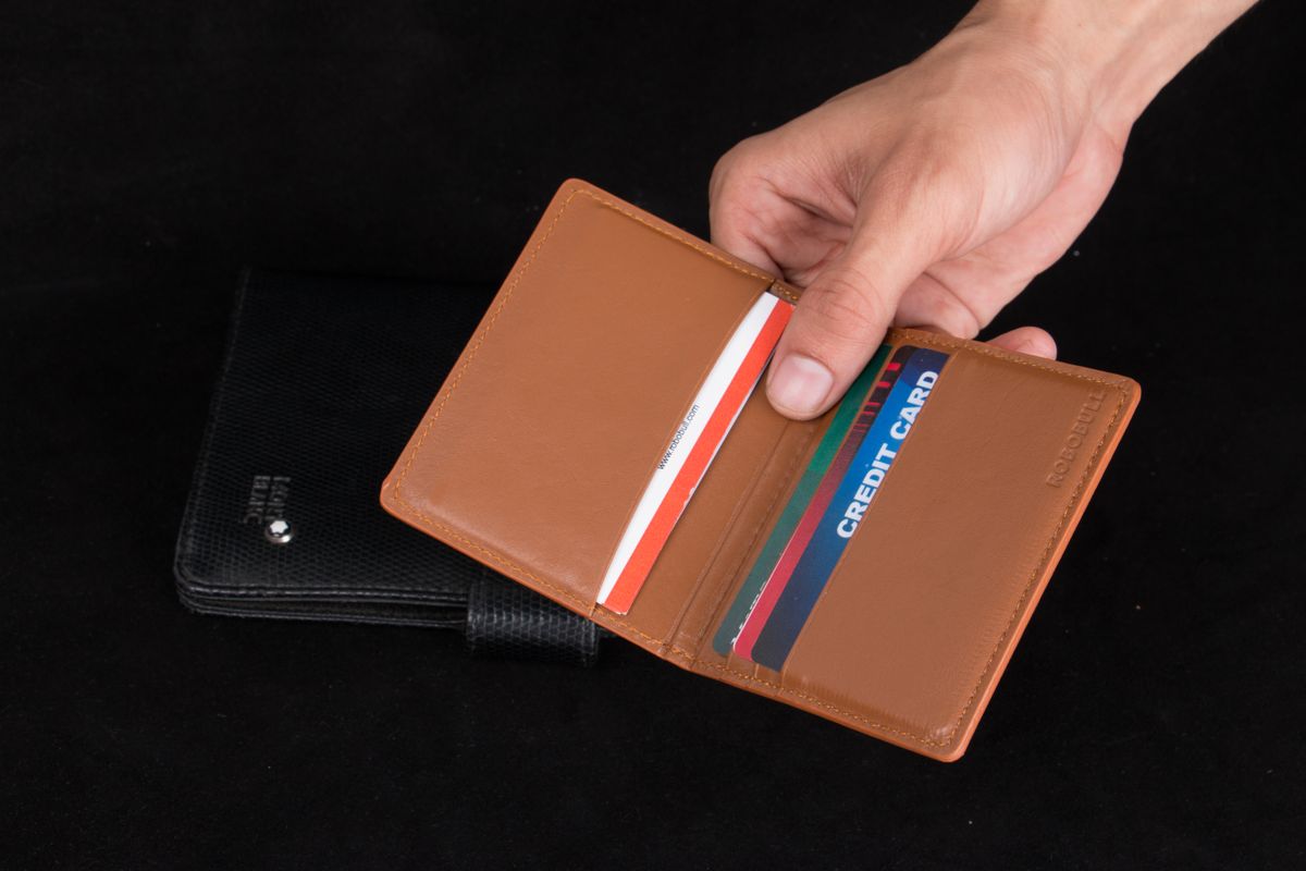 Mâini ținând un portcard din piele maro, cu mai multe carduri colorate