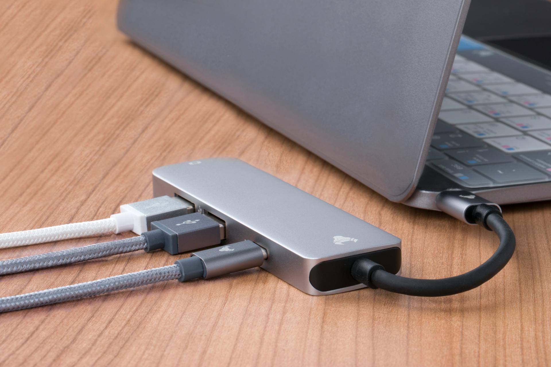 USB hub with multiple connections attached to a sleek laptop on a wooden desk.