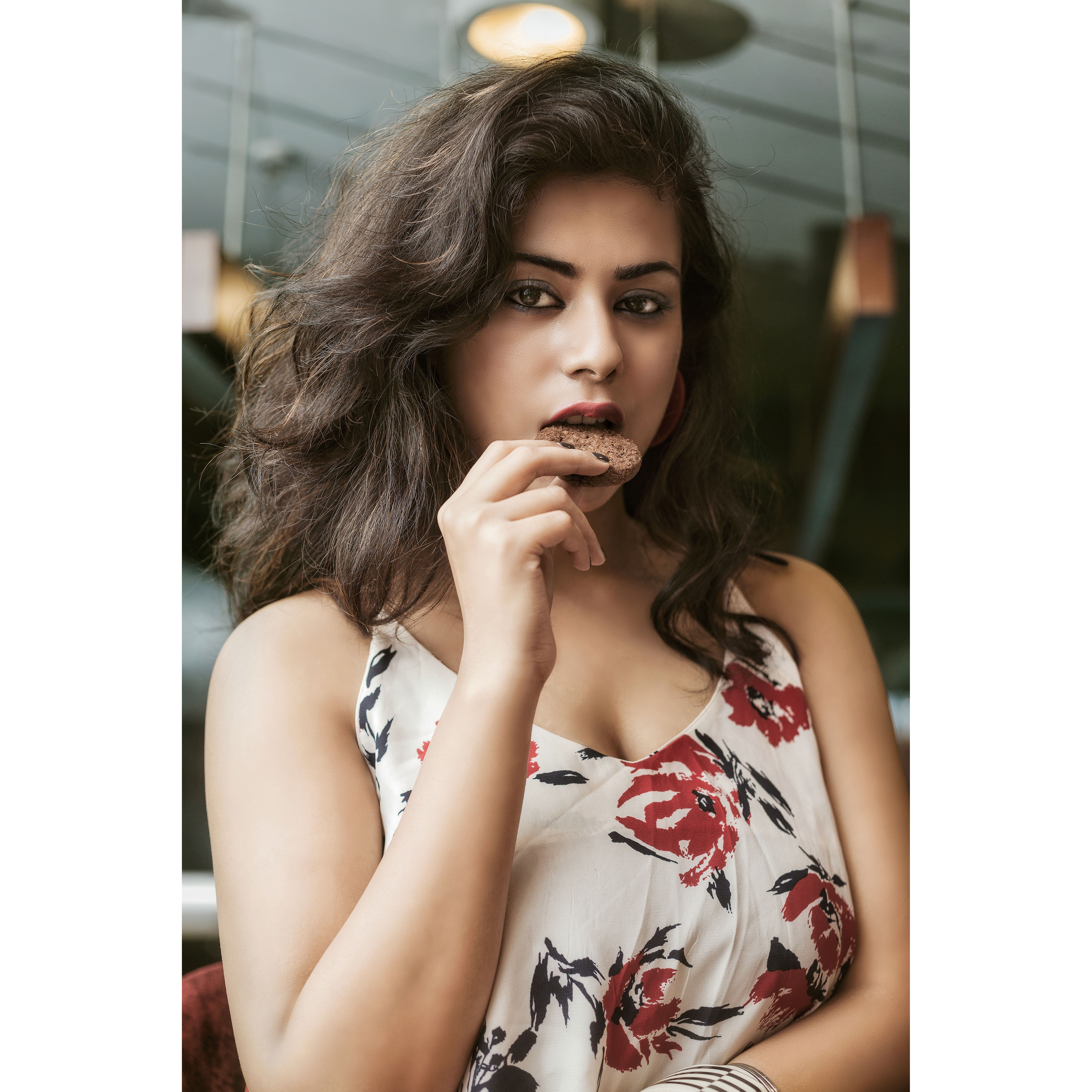 A beautiful woman in a floral top enjoying a cookie indoors.