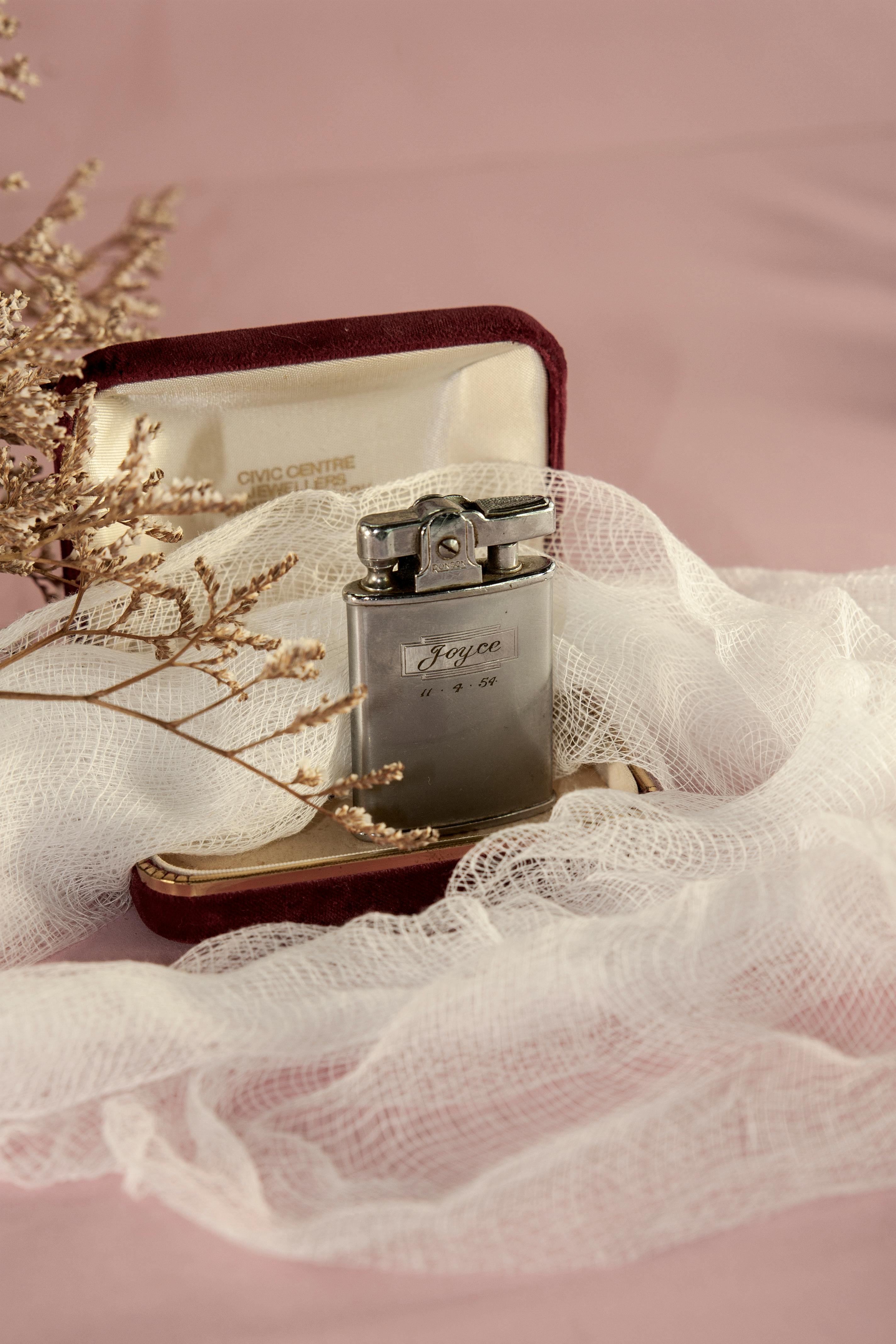 A luxurious silver lighter set against pink fabric and delicate dried flowers.