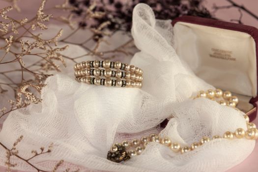 Close-up of pearl jewelry arranged on soft white fabric, with dried flowers.