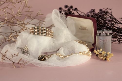 Free Stylish arrangement with pearls, vintage lighter, and accessories on a delicate fabric against a pink background. Stock Photo