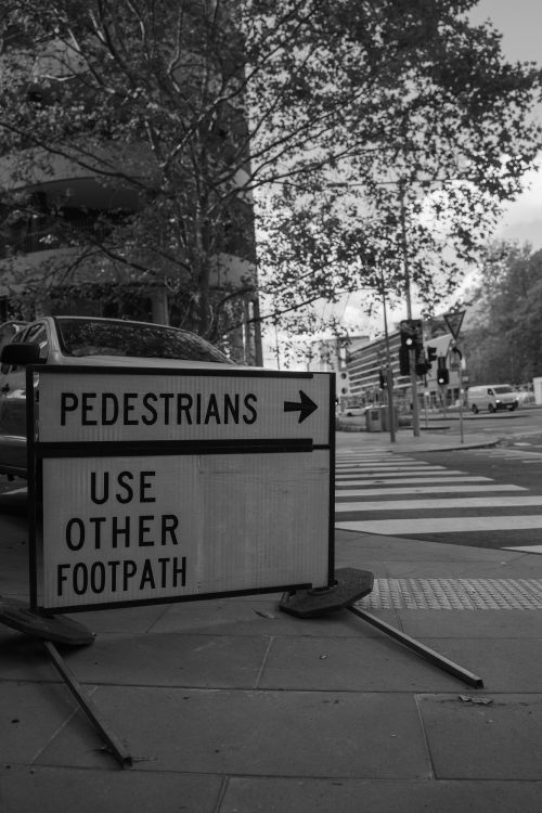 Free Monochrome image of a pedestrian sign directing foot traffic at a city intersection. Stock Photo