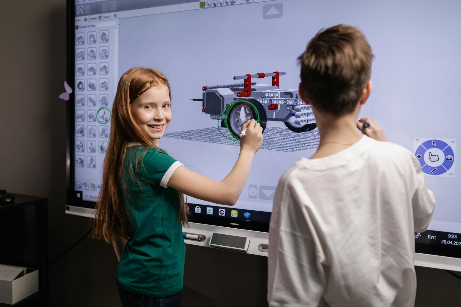 Two children interacting with a digital screen in a classroom setting, learning through technology.