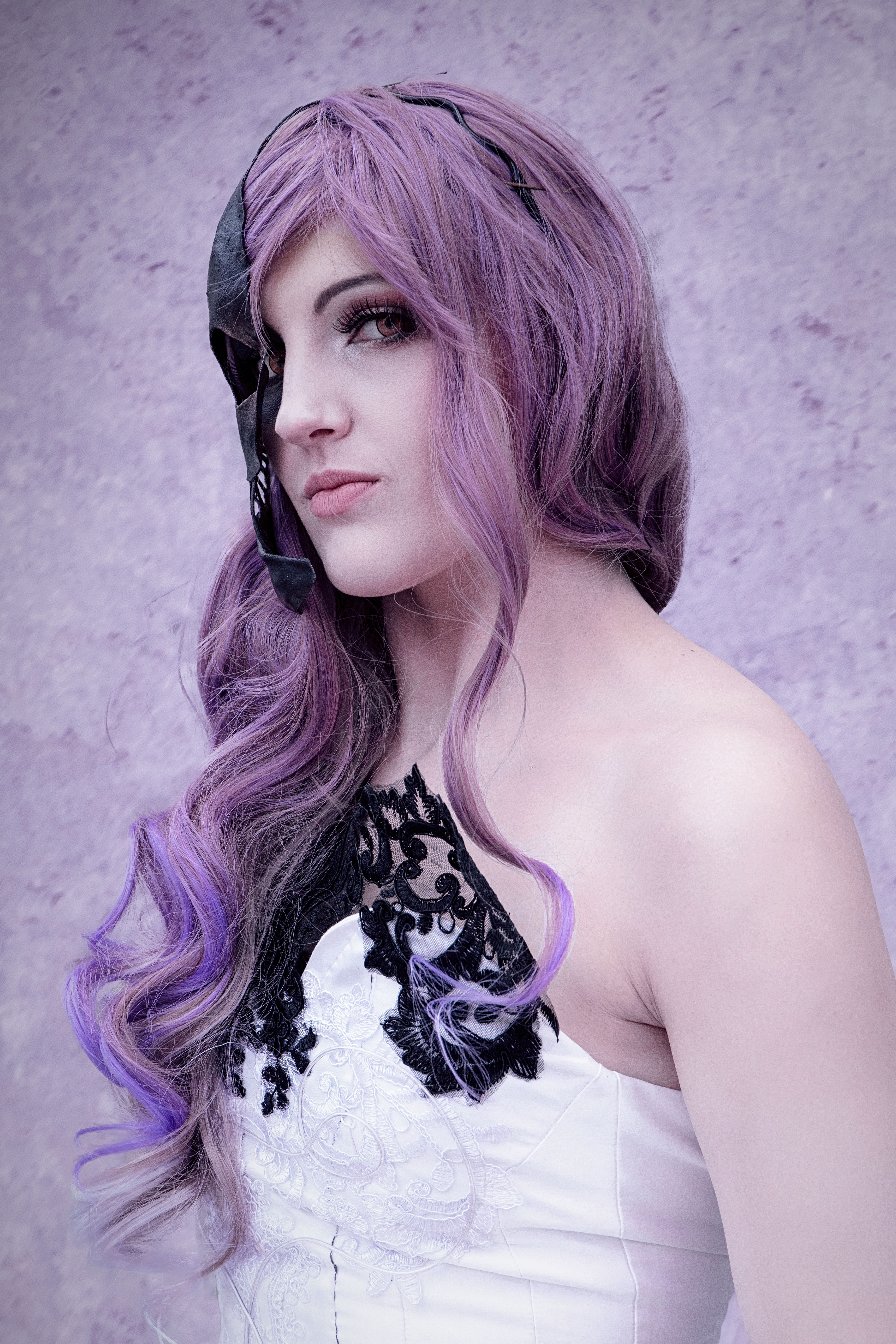 Glamorous woman with purple hair in a gothic cosplay outfit posing elegantly outdoors.