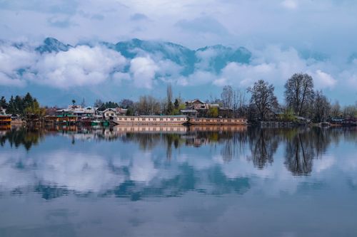 Free Tranquil view of houses reflected in a calm lake with dramatic clouds above. Stock Photo