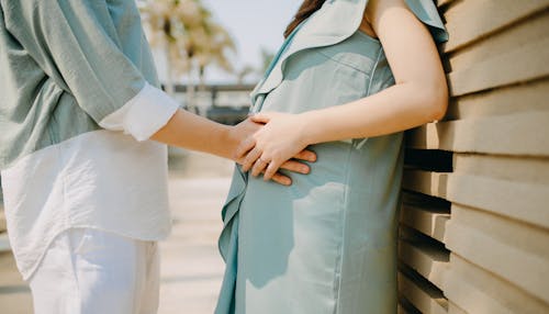 Crop unrecognizable man in summer wear gently touching pregnant wife belly while standing together on sunny street