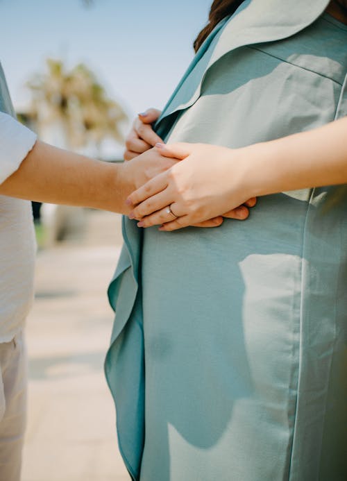 Crop anonymous pregnant female with husband touching belly tenderly while standing together on sunny summer street