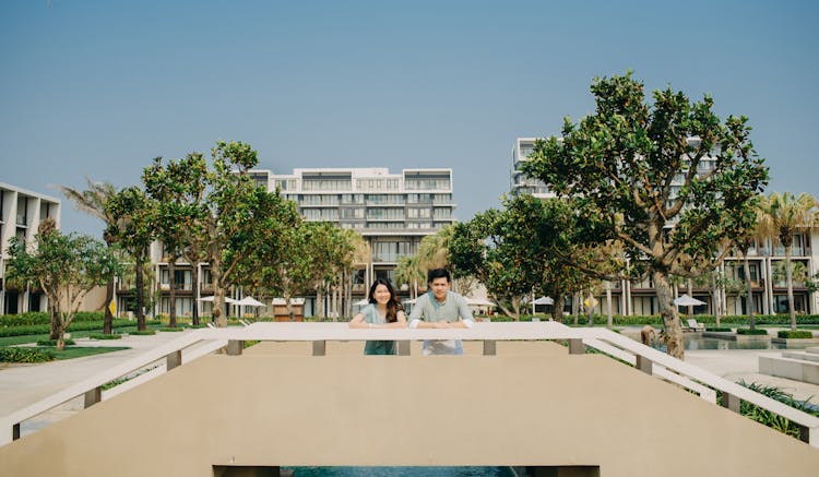 Asian Couple Leaning On Railing Standing On Park Of Hotel