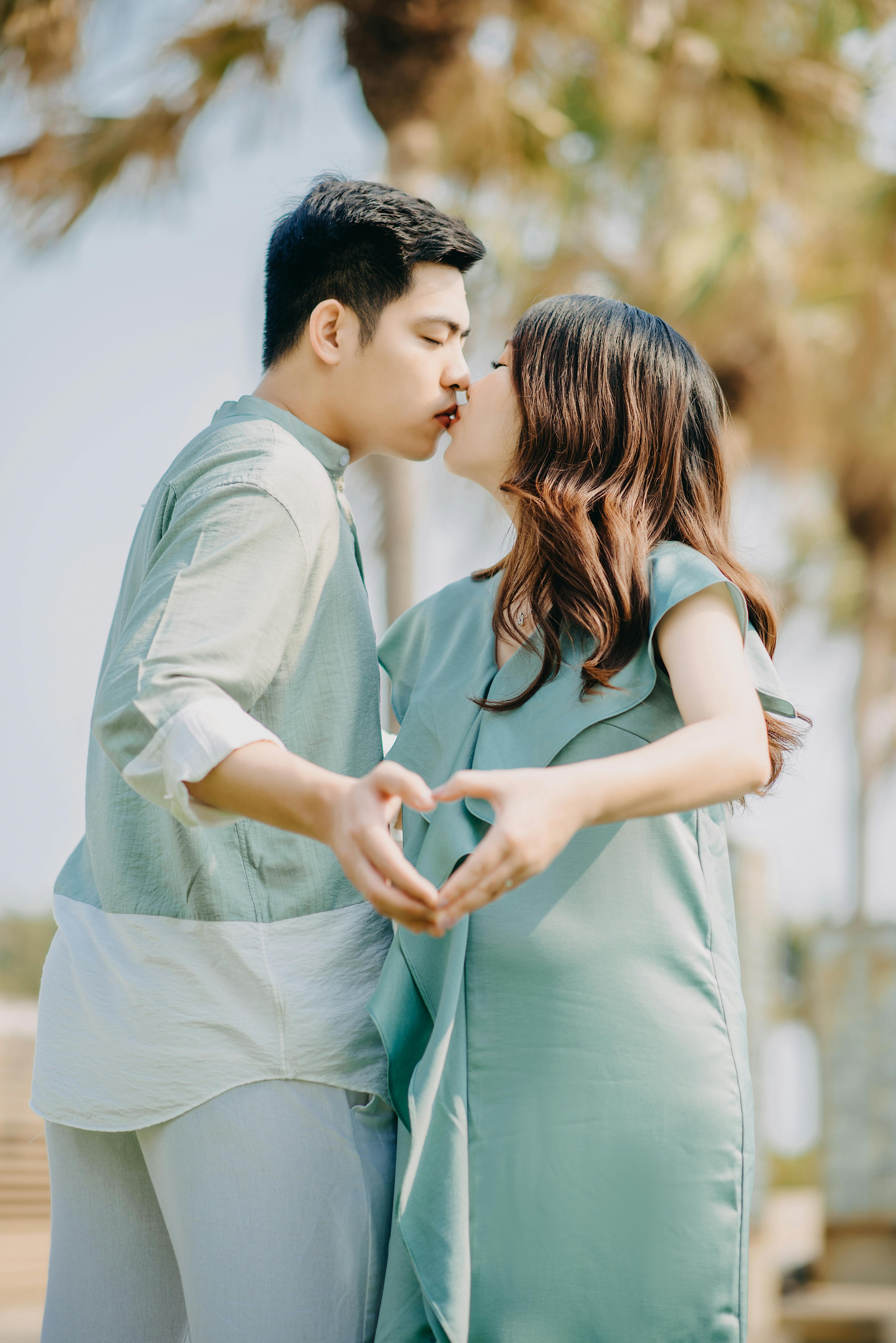 A loving pregnant couple kissing in a sunny park, showing tenderness and connection.
