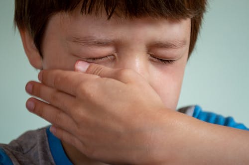 Free Portrait of crop upset little child with brown hair and closed eyes crying and wiping tears from cheek against white background Stock Photo